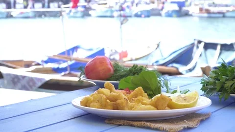 Fried seafood with lemon and arugula on blue table by the sea and small boats Stock Footage 80302928