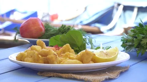 Fried seafood with lemon and arugula on blue table by the sea and small boats Stock Footage 80303032