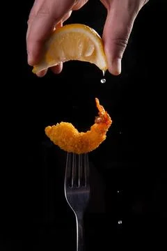 Fried shrimp on a fork is sprinkled with lemon juice. Stock Photos