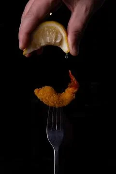 Fried shrimp on a fork is sprinkled with lemon juice. Stock Photos