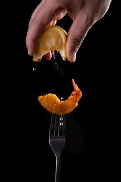 Fried shrimp on a fork is sprinkled with lemon juice. Stock Photos