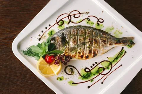 Fried snapper fish with lemon and herbs on white plate Stock Photos