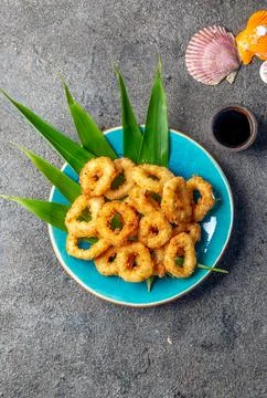 Fried squid rings on blue plate decorated with tropical leaves. Gray concrete Stock Photos