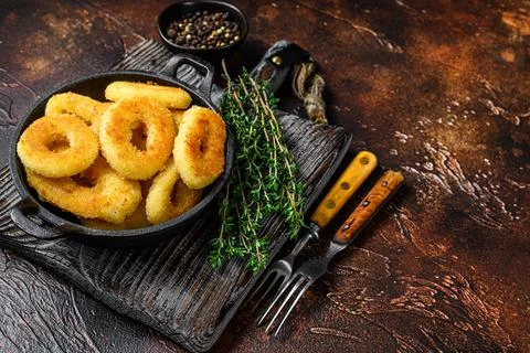 Fried squid rings breaded on a cutting board. Dark background. Top view. Copy Stock Photos