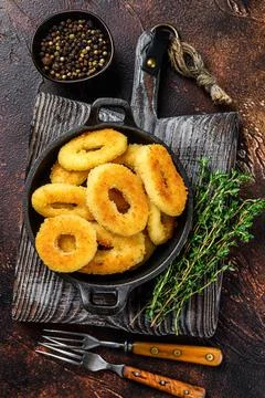 Fried squid rings breaded on a cutting board. Dark background. Top view Stock Photos