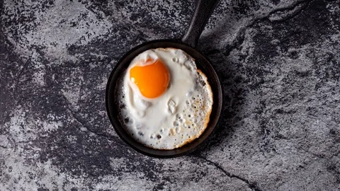 Fried sunny side up egg in iron cast skillet spinning, top view time lapse Video stock 124723741