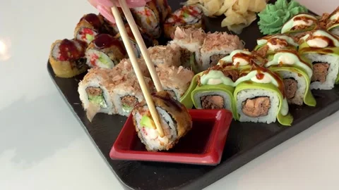 Fried sushi roll dipped into soy sauce beside fresh sushi set on black plate in Stock Footage 346185998