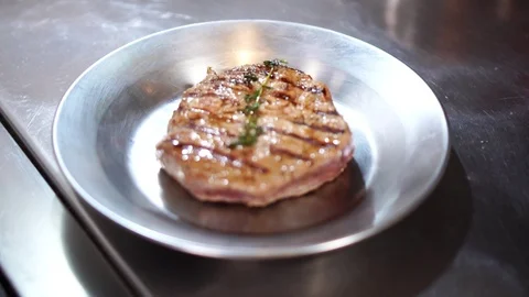 Fried thick piece of beef steak meat on steel plate in slow motion close up view Stock Footage 105895527