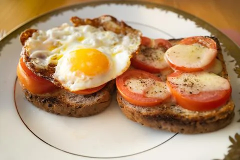 Fried tomatoes with an added egg and cheese on sliced brown toast. Stock Photos