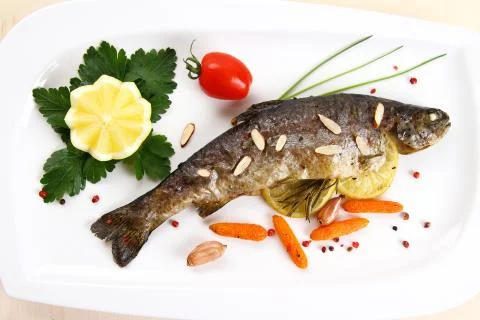 Fried trout with vegetables and split almonds on white plate Stock Photos