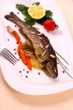 Fried trout with vegetables and split almonds on white plate Stock Photos