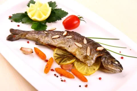 Fried trout with vegetables and split almonds on white plate Stock Photos