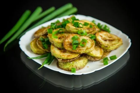 Fried zucchini in circles with fresh herbs in a plate on a black Stock Photos