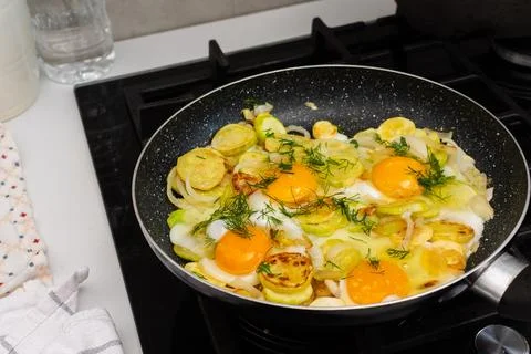 Fried zucchini is cooked with scrambled eggs in a pan on a stovetop. The scen Stock Photos