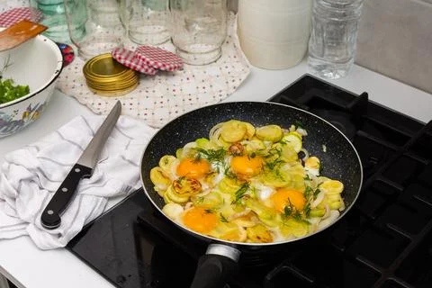 Fried zucchini is cooked with scrambled eggs in a pan on a stovetop. The scen Stock Photos