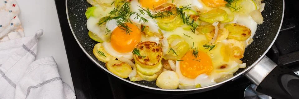 Fried zucchini is cooked with scrambled eggs in a pan on a stovetop. The scen Stock Photos