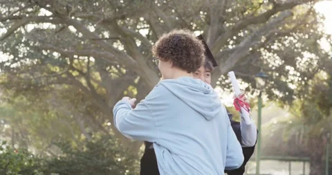 Friend approaching, graduate hugging under oak tree while checking diploma Stock Footage 343514100