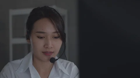 Friendly Asian Customer Service with headset working on desktop computer Stock Footage 128314140