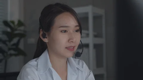 Friendly Asian Customer Service with headset working on desktop computer Video stock 128352175