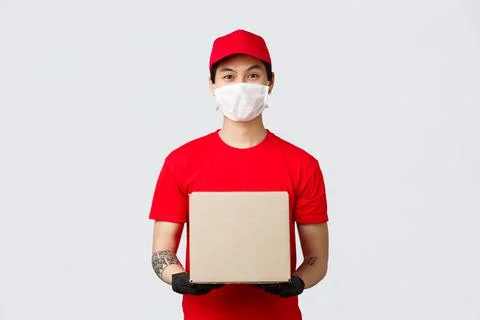 Friendly asian delivery guy with box parcel waiting for client open door 写真素材