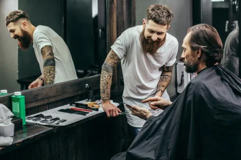 Friendly barber smiling while client showing screen of smartphone Stock Photos