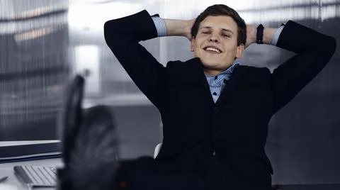 Friendly businessman in a black suit is sitting at the desk at his workplace Stockfoto's