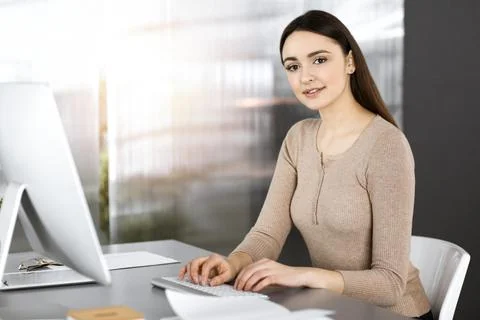 Friendly casual dressed business woman is working on her computer, while sitting Stock Photos