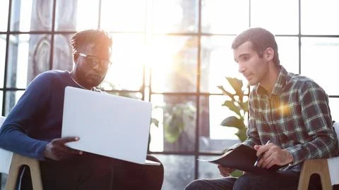 Friendly colleagues chat while sitting in the office, promising young manager Stock Photos
