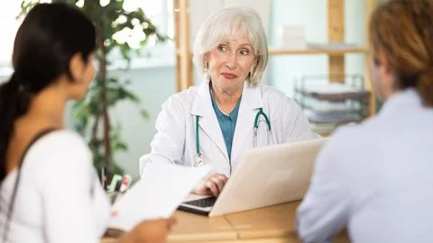 Friendly elderly doctor talking to young couple at table Stock Photos