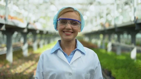 Friendly female scientist smiling at camera in greenhouse, breeding research Stockbeeldmateriaal 118936458