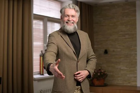Friendly gray-haired man extends his hand in greeting at home Stock Photos