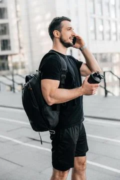 Friendly man in black clothes talking on the phone, smiling and looking away Stock Photos