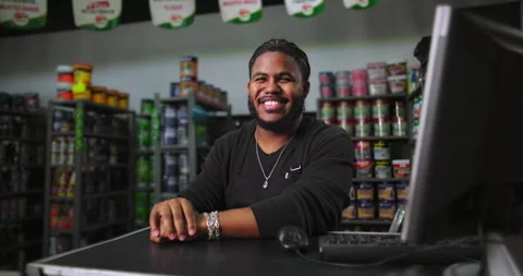Friendly man sitting at paint store counter with organized shelves of paint cans Stock Footage 318743890