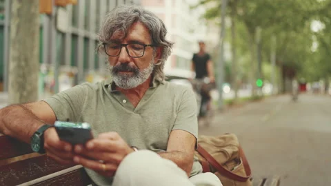 Friendly middle-aged man with gray hair and beard wearing casual clothes sits on Stock Footage 227030286