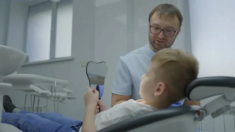 Friendly pediatric dentist talking to her little patient. Boy and the dentist in Video stock 230504819