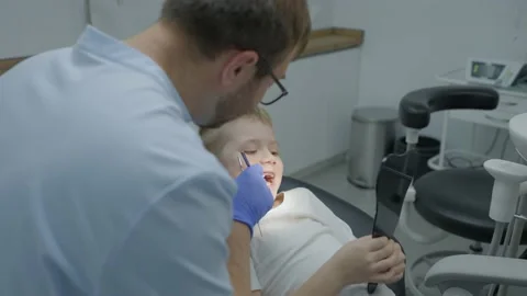 Friendly pediatric dentist talking to her little patient. Boy and the dentist in Stock Footage 230505029