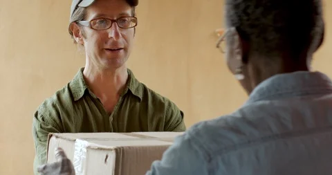 Friendly postal courier delivery man giving a box to a black woman home owner Video stock 91863590