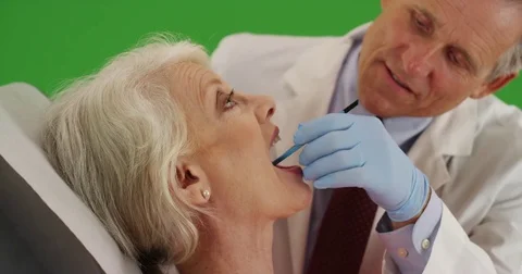 Friendly senior dentist examining elderly woman's teeth on green screen Stock Footage