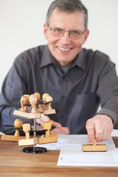 Friendly smiling clerk stamping a document at a desk in an office - focus on Stock Photos