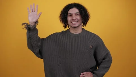 Friendly smiling man waving hand and making hello gesture while standing in Stock Footage 260566206