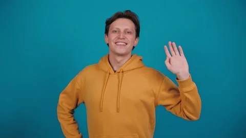 Friendly smiling man waving hand and making hello gesture while standing in Stock Footage 263292884