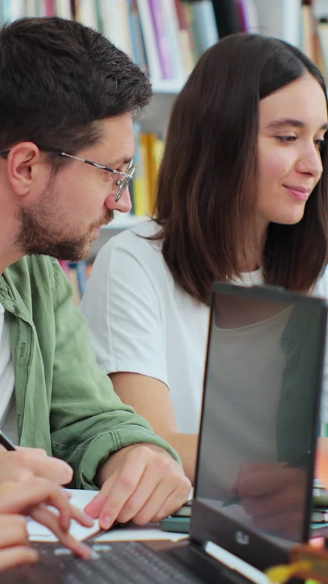 Friendly students sit at desk in library writing, discuss collaborative project Stock Footage 345144500