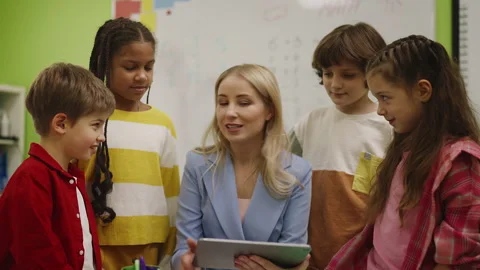 Friendly teacher helping pupils with project using tablet, classroom learning Stock Footage 333585530