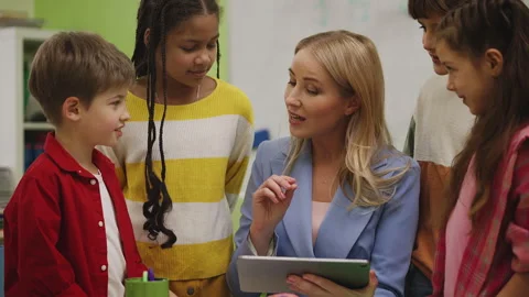 Friendly teacher helping pupils with school project on tablet in classroom Stock Footage 335683689
