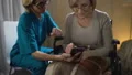 Friendly volunteer teaching woman in wheelchair to use smartphone, nursing home HD Footage