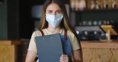 Friendly waitress in protective mask posing at cafe with menu in hands 스톡 동영상 164257905
