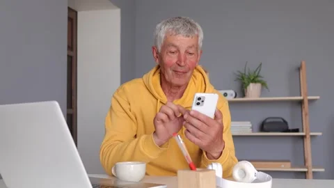 Friendly white haired mature man wearing yellow hoodie using his mobile phone Stockbeeldmateriaal 292760779