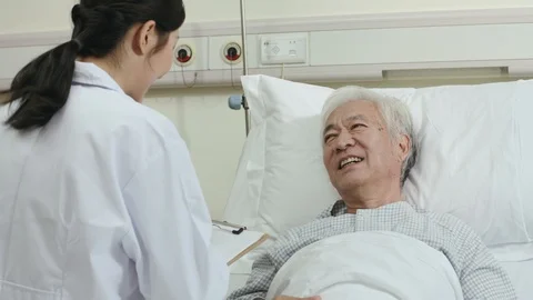 Friendly young asian doctor talking to senior patient in hospital ward Stock Footage