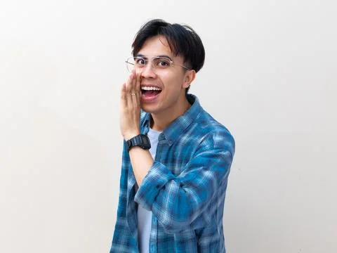 A friendly young Asian man looking at the camera while whispering a secret .. Stock Photos
