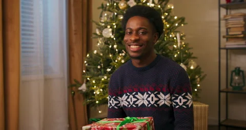 Friendly young guy of African appearance sitting on the floor near the Christmas 스톡 동영상 211658054